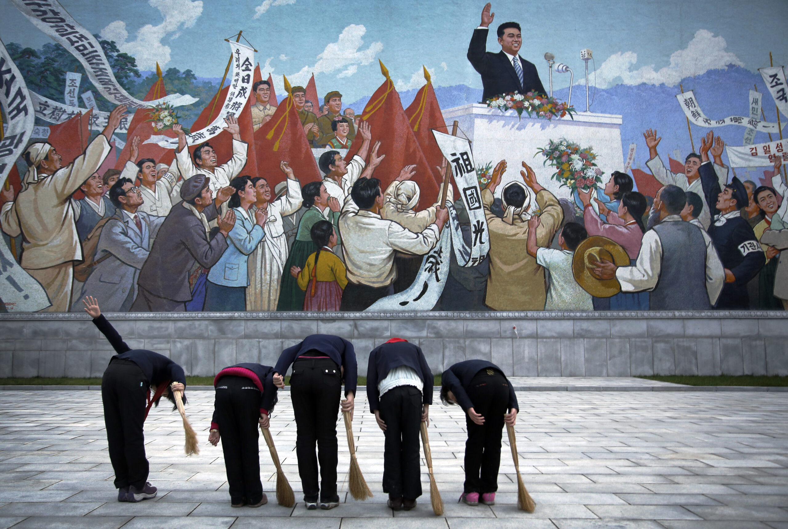 North Korean school girls holding brooms bow to pay their respects toward a mural which shows the late North Korean leader Kim Il Sung delivering a speech, before sweeping the area surrounding this mural on Tuesday, Dec. 1, 2015, in Pyongyang, North Korea, one of over 70 photos that will be on display at Objectifs in Singapore. (AP Photo/Wong Maye-E)